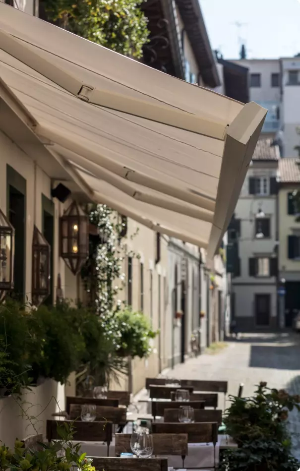 Veduta di una strada tranquilla con tende da sole bianche, lampade vintage e piante decorative lungo i muri, creando un'atmosfera accogliente.