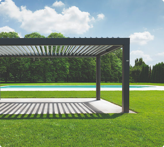 Una pergola moderna in metallo con strisce, affacciata su un ampio prato verde e una piscina, sotto un cielo blu.